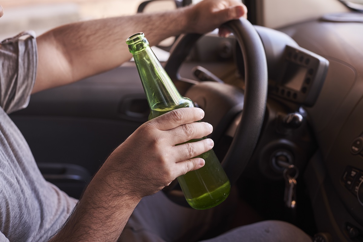 man driving while holding a bottle of beer
